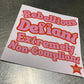 Sticker with text 'Rebellious Defiant Extremely Non-Compliant' on a metallic surface