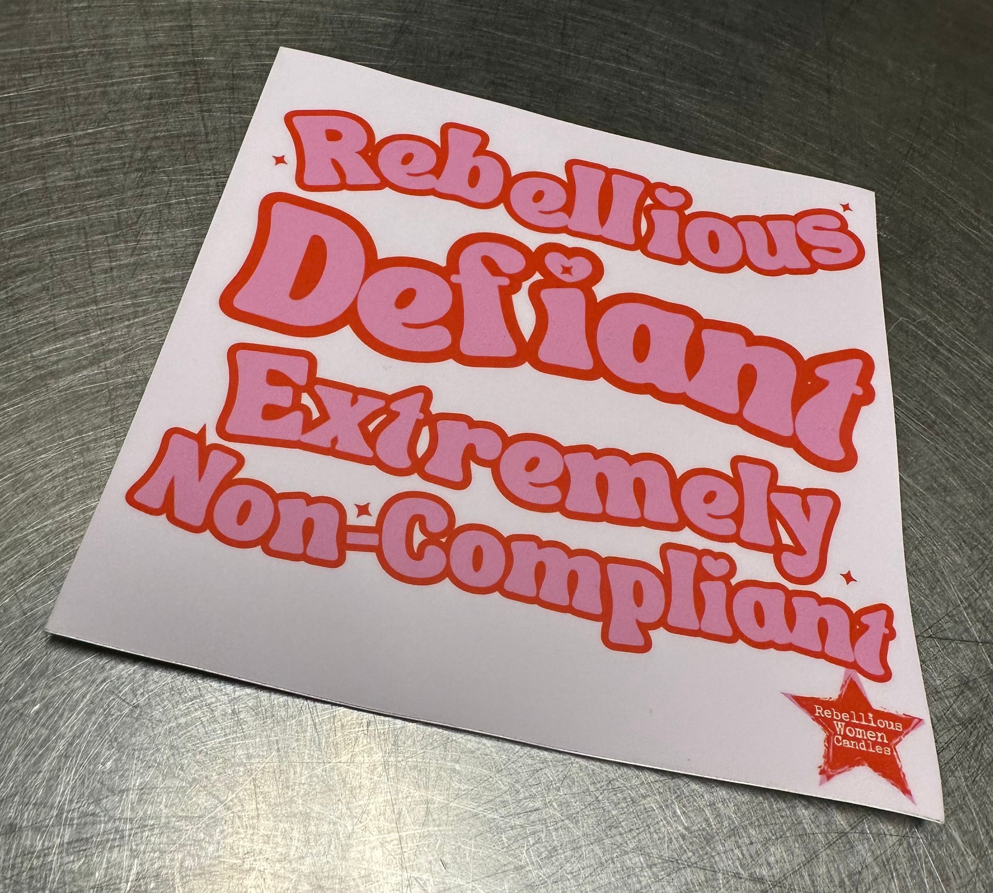Sticker with text 'Rebellious Defiant Extremely Non-Compliant' on a metallic surface